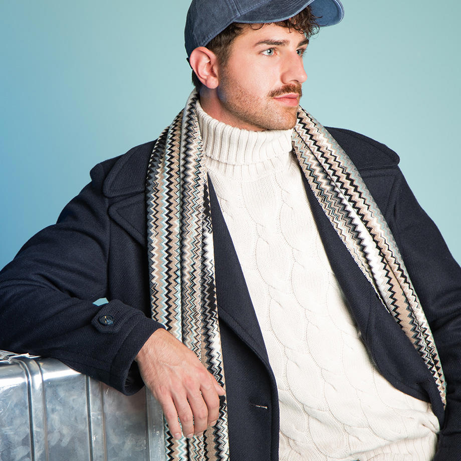 Mann in dunkelblauem Mantel und weißem Rollkragenpullover mit gemustertem Schal