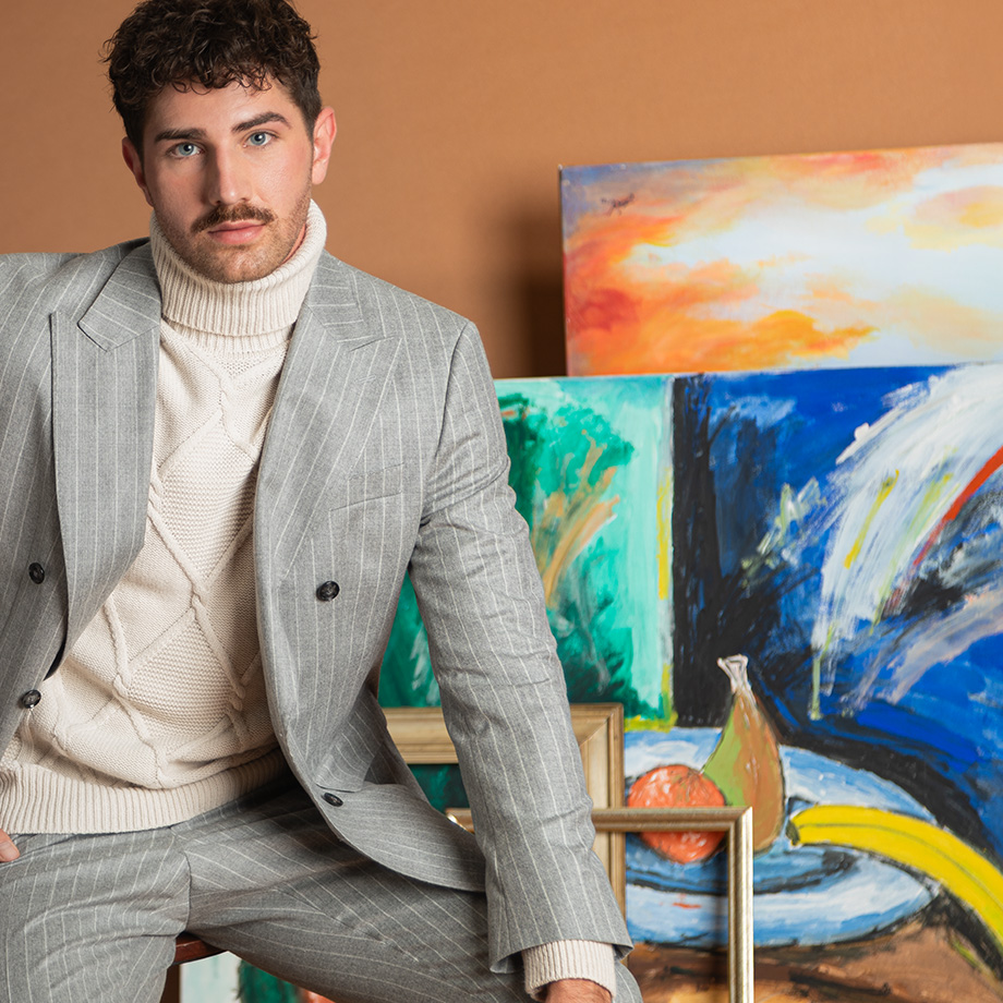 Mann im grauen Nadelstreifenanzug mit cremefarbenem Rollkragenpullover, leger in Atelier sitzend