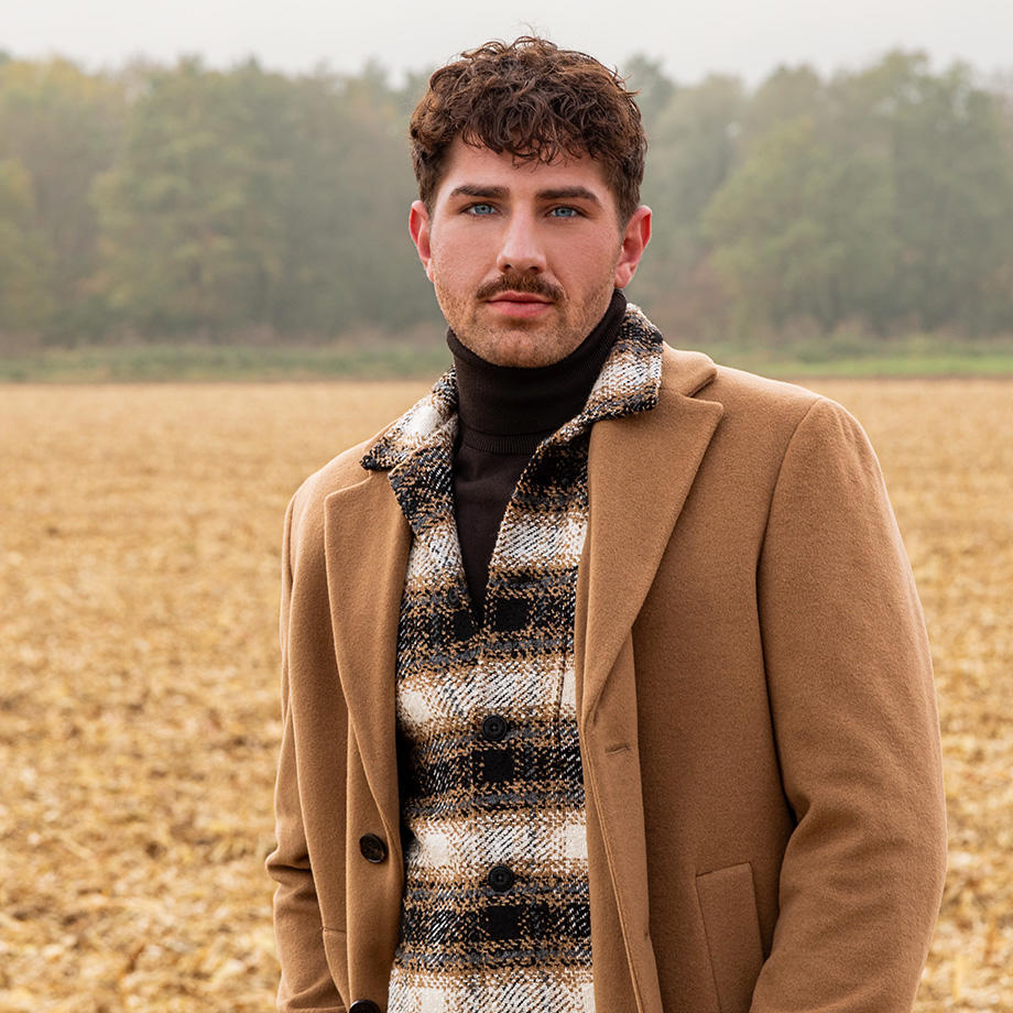 „Mann im beigen Wollmantel und kariertem Hemd mit Rollkragenpullover auf freiem Feld“