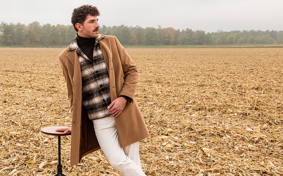 „Mann im beigen Wollmantel und kariertem Hemd mit Rollkragenpullover auf freiem Feld“