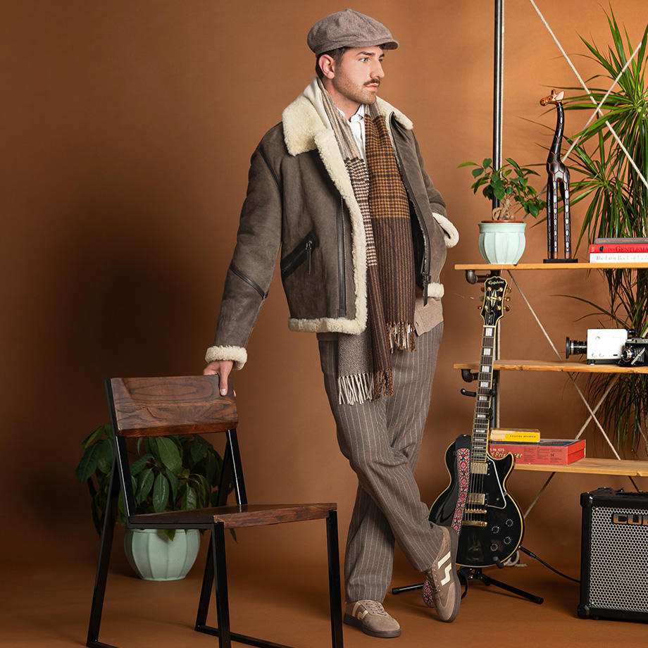 Mann in brauner Lammfelljacke mit Schiebermütze und gestreifter Anzughose, lässig präsentiert