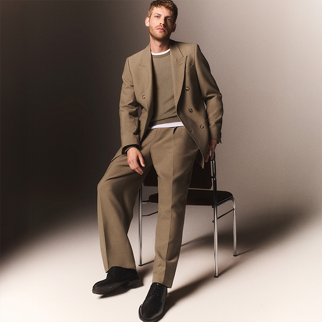 Hellbrauner Anzug, doppelreihig, aus Wolle, mit weißem Shirt getragen, Mann sitzt lässig auf Stuhl