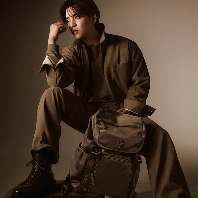 Mann in olivgrünem Freizeitanzug mit passendem Rucksack aus Stoff, lässig sitzend