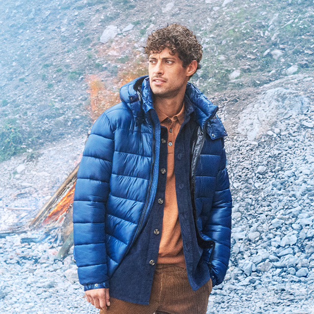 Mann in blauer, gesteppter Winterjacke über braunem Hemd im Freien