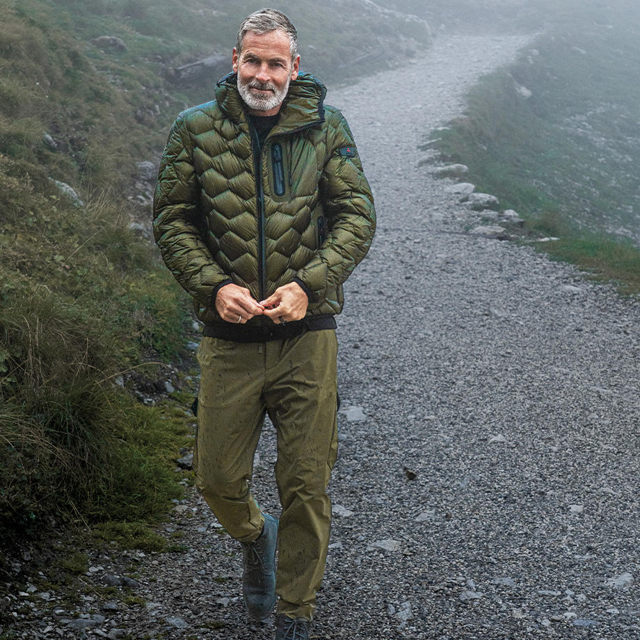 Mann in olivgrüner Daunenjacke und Cargohose auf Wanderweg