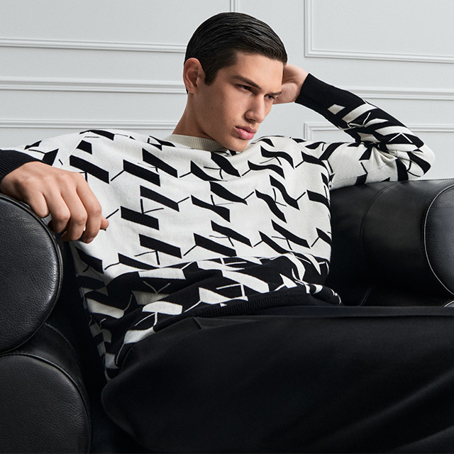 Mann in schwarz-weiß gemustertem Strickpullover mit geometrischem Design, auf Sofa liegend