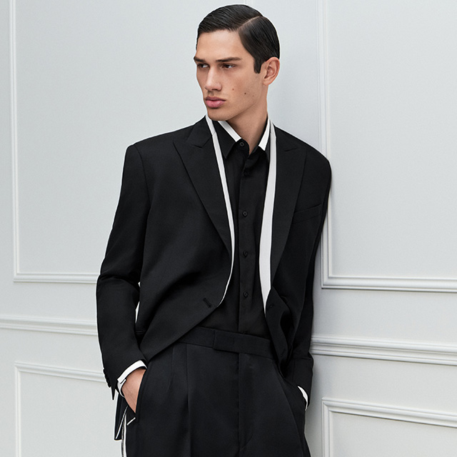 Schwarzes Sakko mit kontrastierendem weißem Besatz, kombiniert mit Hemd und Bundfaltenhose, smarter Fashion-Look.