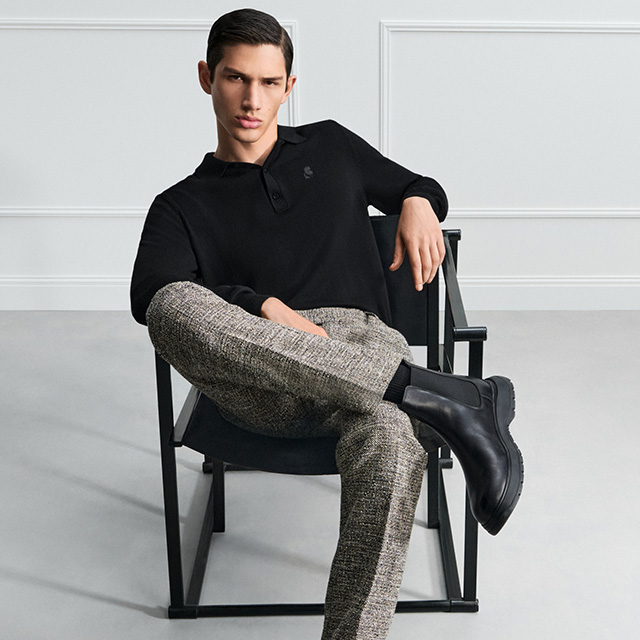 Mann in schwarzem Poloshirt und melierter Stoffhose, sitzend mit Chelsea-Boots