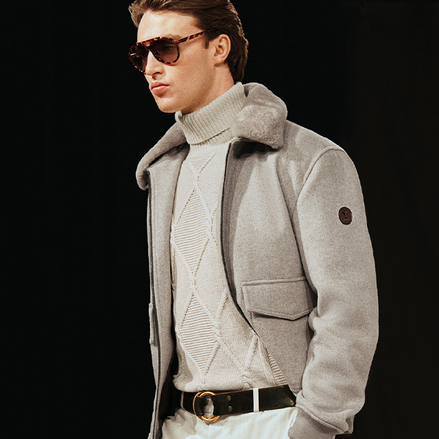 Hellgraue Jacke mit Fellkragen, kombiniert mit Strickpullover im Rautenmuster, stilvoller Winter-Look.