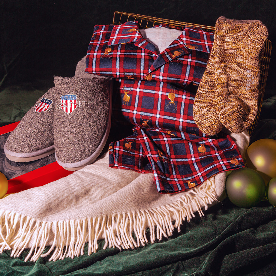 Rotes kariertes Pyjama-Set mit Hirschmuster auf Wollschal, graue Filzpantoffeln und braune Stricksocken.