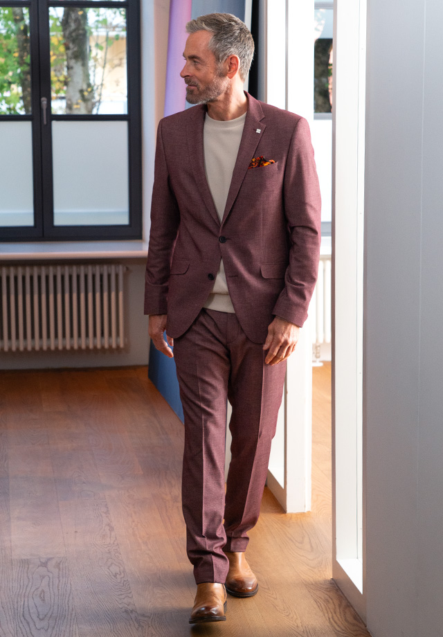 Mann im bordeauxfarbenen Anzug mit beigem Pullover im Büro