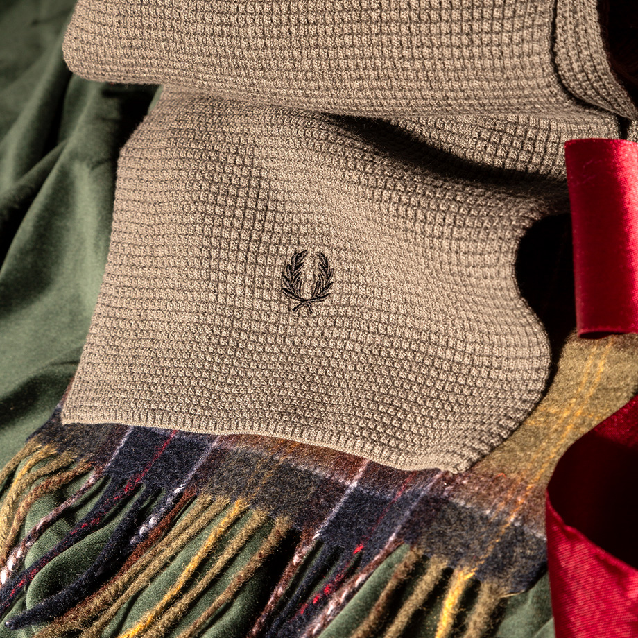 Brauner Schal mit Waffelmuster und gesticktem Logo, auf grünem Stoff präsentiert