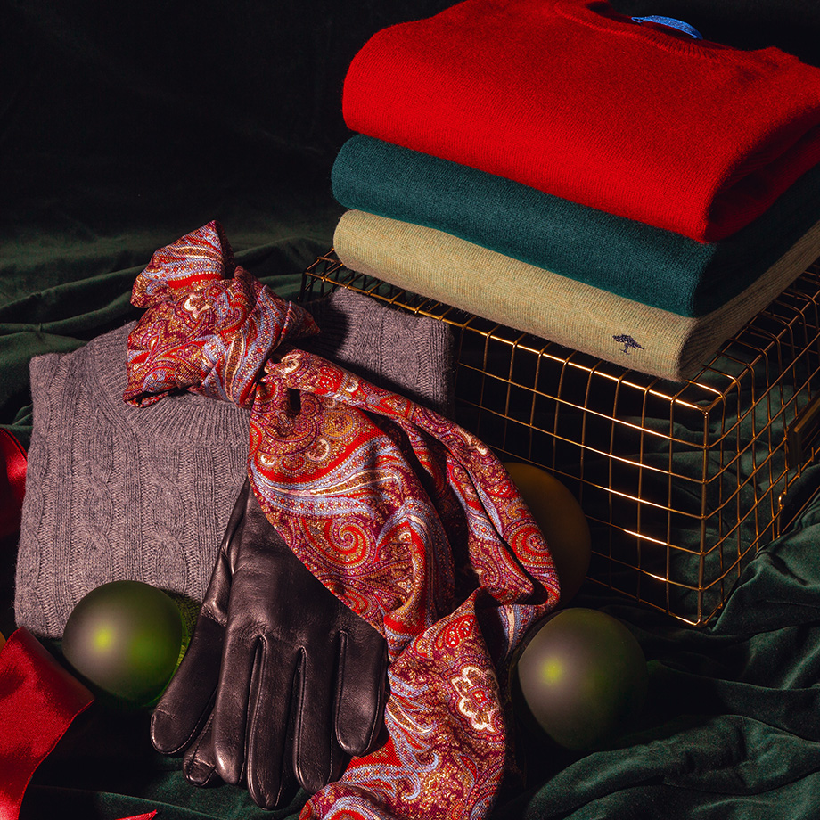 Grauer Strickpullover aus Wolle mit schwarzem Lederschal, drapiert auf goldener Ablage