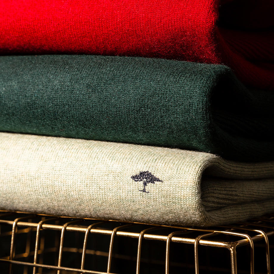 Strickpullover in Rot, Grün und Beige, gefaltet, Akzent auf Logo-Stickerei, präsentiert auf Metallregal