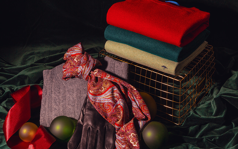 Gestapelte Pullover in Rot, Grün, Beige auf Gitterkorb mit Paisley-Schal und Lederhandschuhen