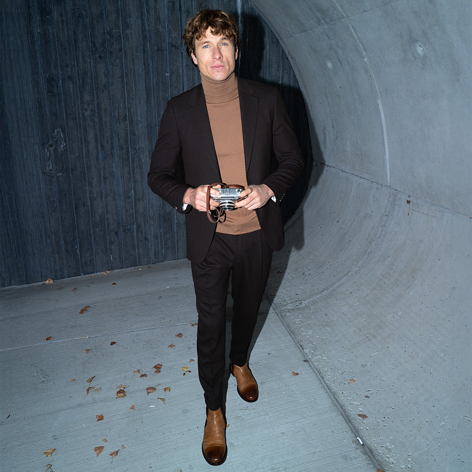 Mann im dunkelbraunen Anzug, Rollkragenpullover in Beige, draußen mit Kamera
