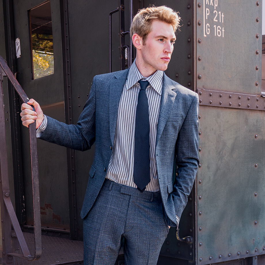 Mann in blauem Anzug mit Streifenhemd und Krawatte, leger an Bahntreppe gelehnt