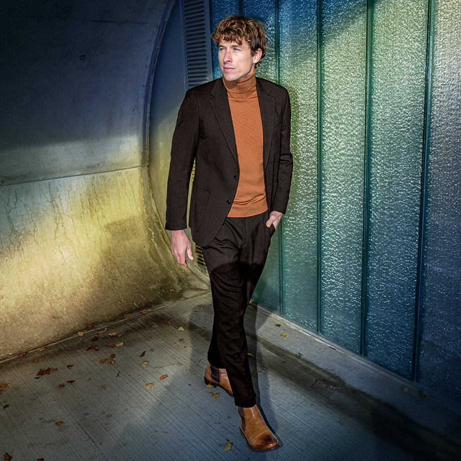 Mann in braunem Anzug mit orangefarbenem Rollkragenpullover, elegant präsentiert