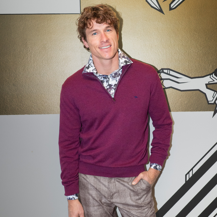 Eleganter Mann in bordeauxfarbenem Strickpullover mit gemustertem Hemd und karierter Hose, lässig präsentiert