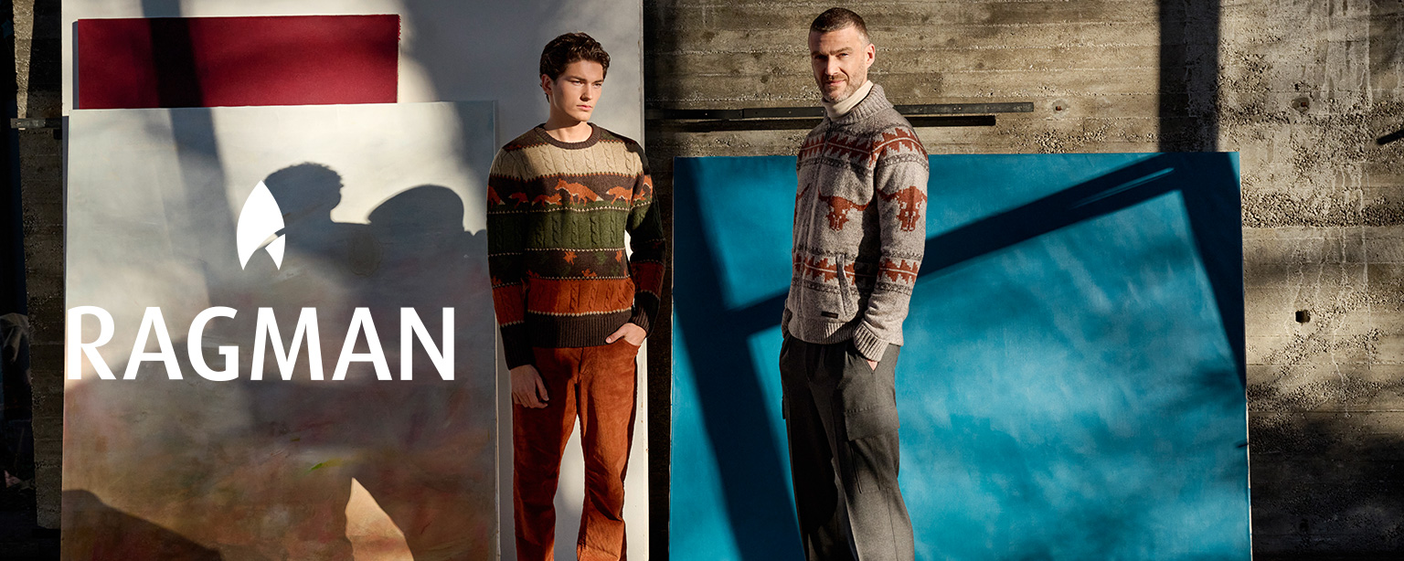 Herr in brauner Suede-Jacke mit grauem Strick-Cardigan und gestreifter Krawatte vor Backsteinhintergrund