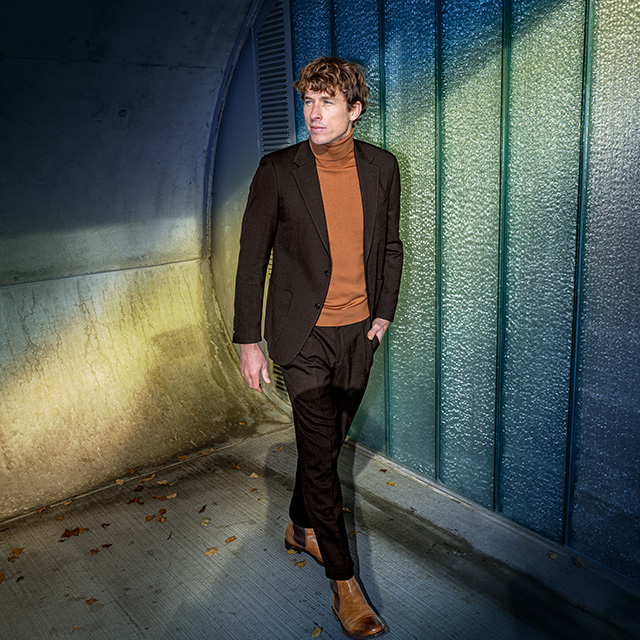 Herr in dunkelbraunem Anzug und cognacfarbenem Rollkragenpullover, eleganter Look