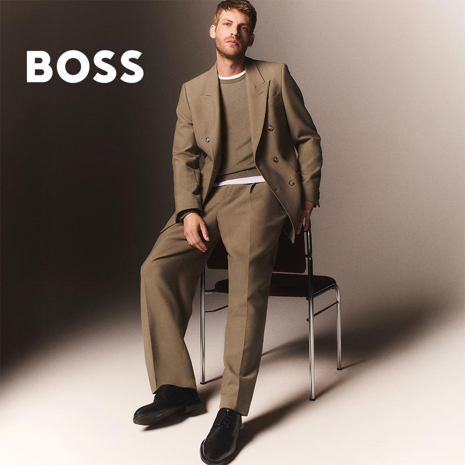 Mann in beigem Anzug mit Strickpullover, lässig auf Stuhl sitzend