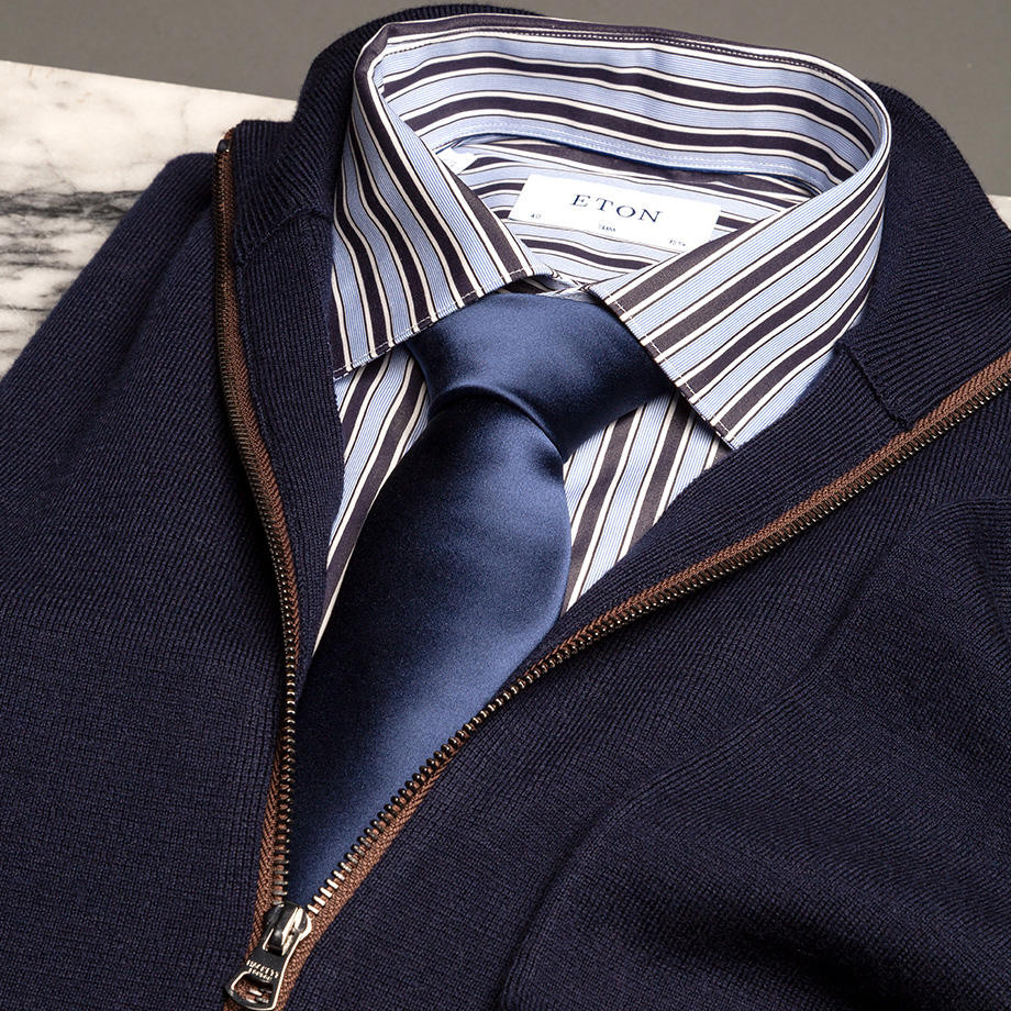 Gestreiftes Hemd in Blau-Weiß mit dunkelblauer Krawatte unter marineblauem Strickpullover mit Reißverschluss
