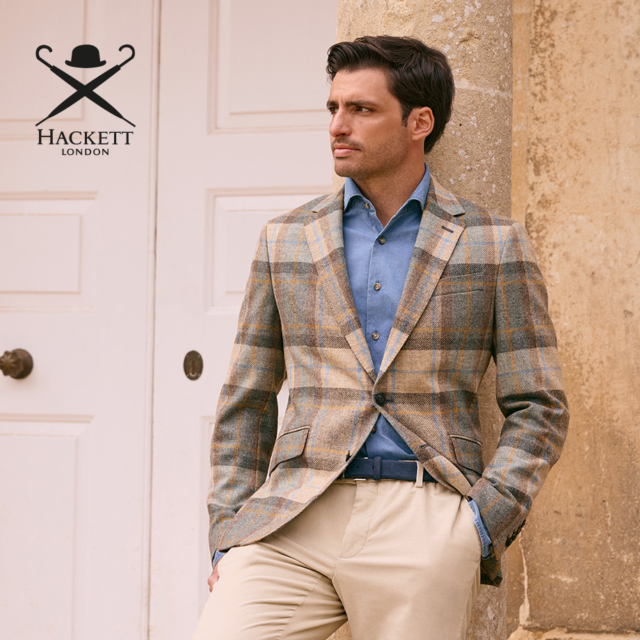 Mann in kariertem Sakko und hellblauem Hemd, lässig vor Gebäude stehend