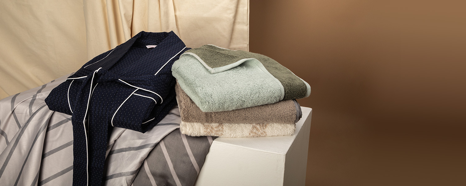 Dunkelblauer Herren-Pyjama mit weißen Akzenten auf gestreifter Bettwäsche drapiert