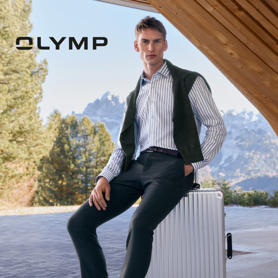 Mann in gestreiftem Business-Hemd mit Pullover über den Schultern, sitzt auf Koffer im Freien