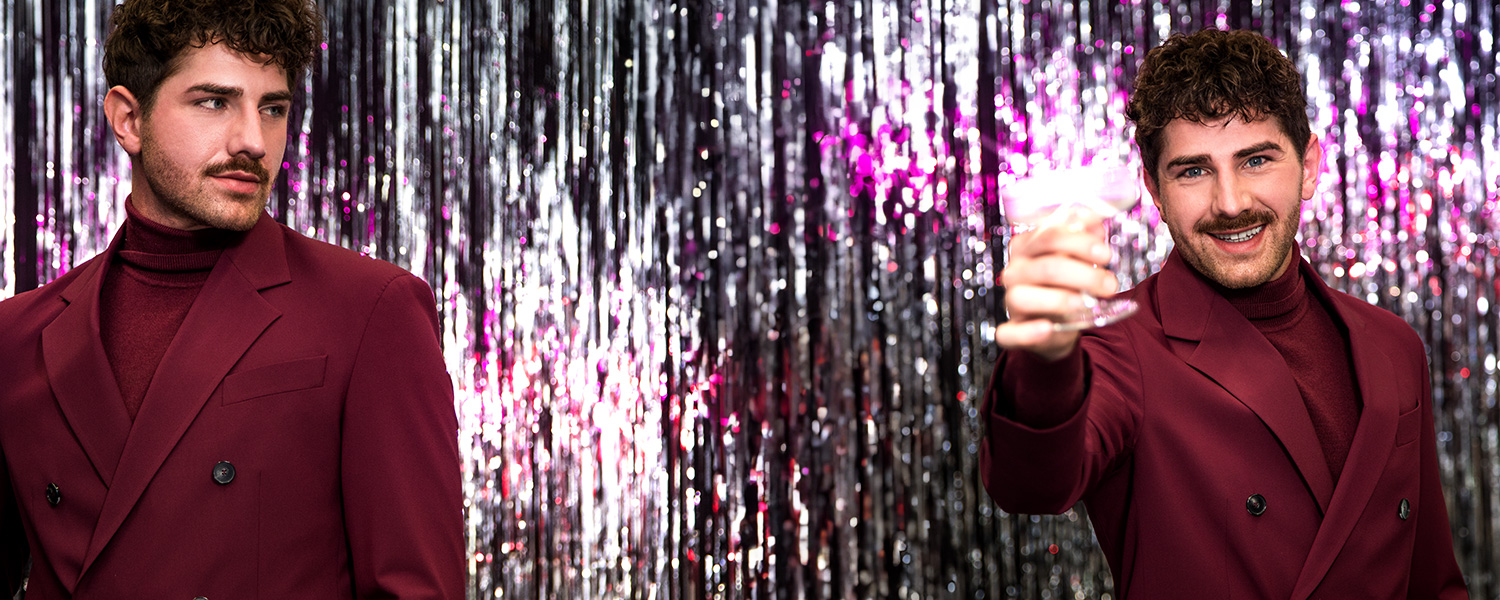 Mann in weinrotem Anzug und Rollkragenpullover, festlich gekleidet mit silberner Hintergrunddekoration