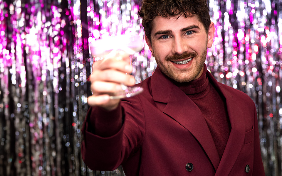 Mann im weinroten Anzug mit Rollkragenpullover, festlich mit Getränk