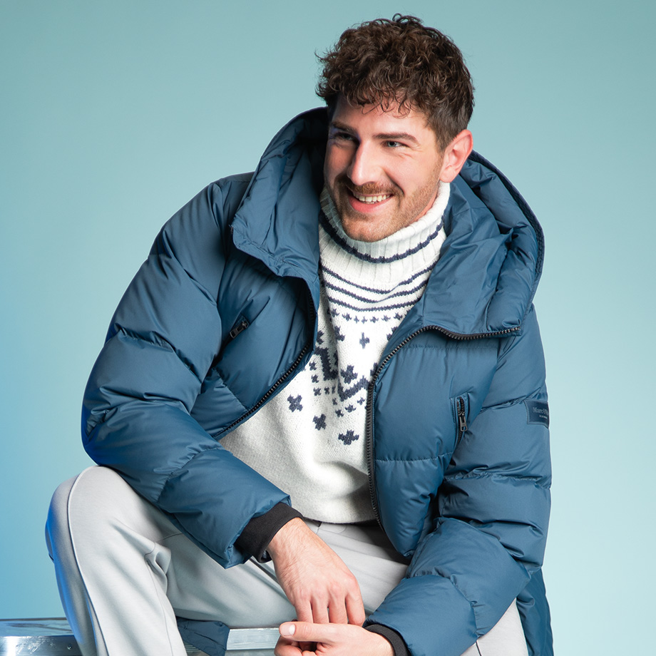 Mann in blauer Daunenjacke und Norwegerpullover, sitzend und lächelnd