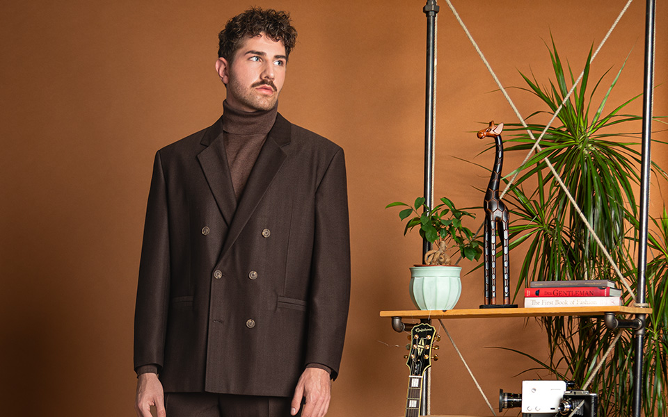 Eleganter Mann im braunen Anzug mit Rollkragenpullover, stehend vor Regal im Wohnzimmer