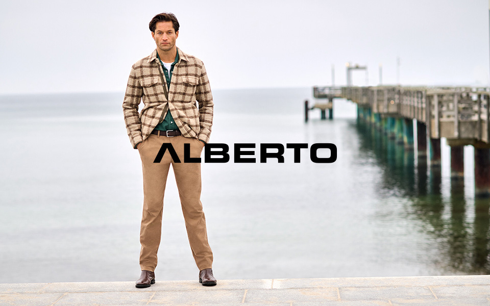 Mann in kariertem Sakko und grüner Freizeithemd mit beigen Chinos, am Wasser stehend