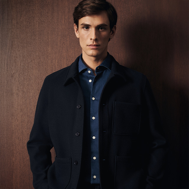 Mann in dunkelblauem Overshirt und marineblauem Hemd, elegant getragen vor Holzwand