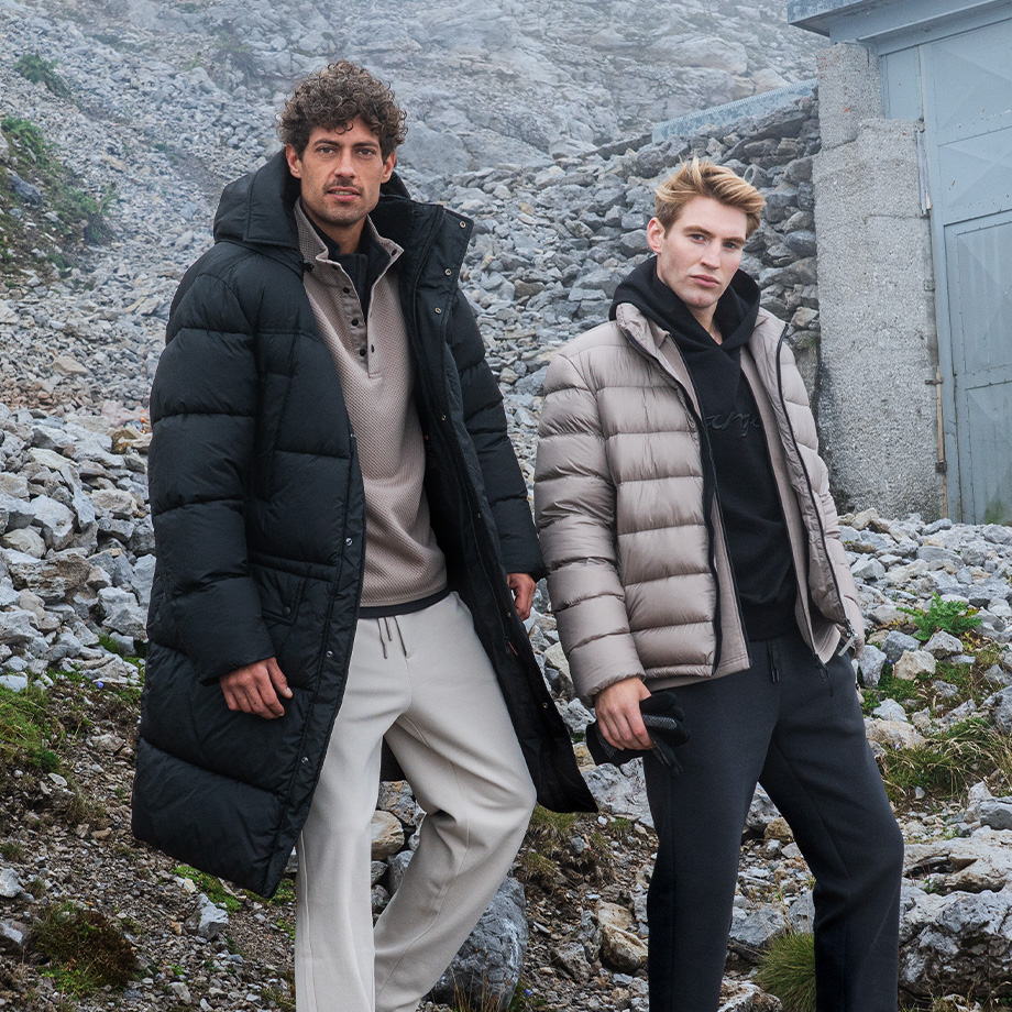 Männer in schwarzen und beigen Daunenjacken im Freien auf einem felsigen Pfad