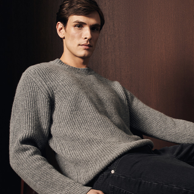 Grau melierter Strickpullover aus Wolle, klassischer Schnitt, leger getragen von sitzendem Mann