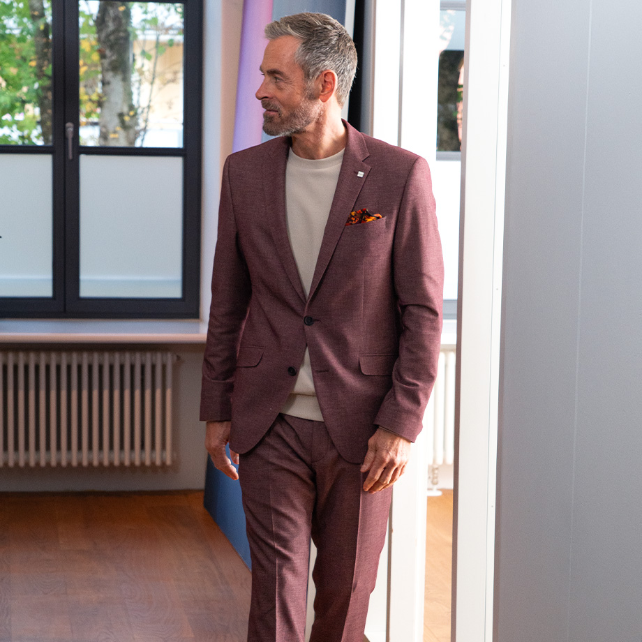 Mann in bordeauxfarbenem Anzug aus Wolle-Mix, leger mit beigem Pullover getragen