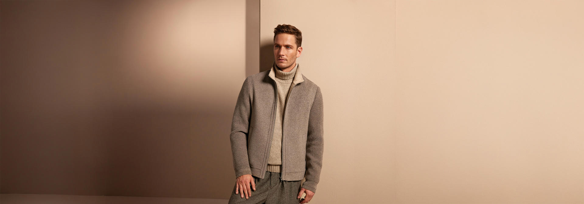 Hellgrauer Strickpullover mit Reißverschlussjacke, Mann entspannt stehend, minimalistischer Hintergrund