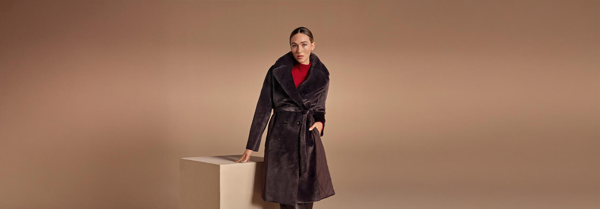 Milestone – Dunkler Fellmantel mit Bindegürtel, kombiniert mit rotem Rollkragen und Lederstiefeln, eleganter Winter-Look.