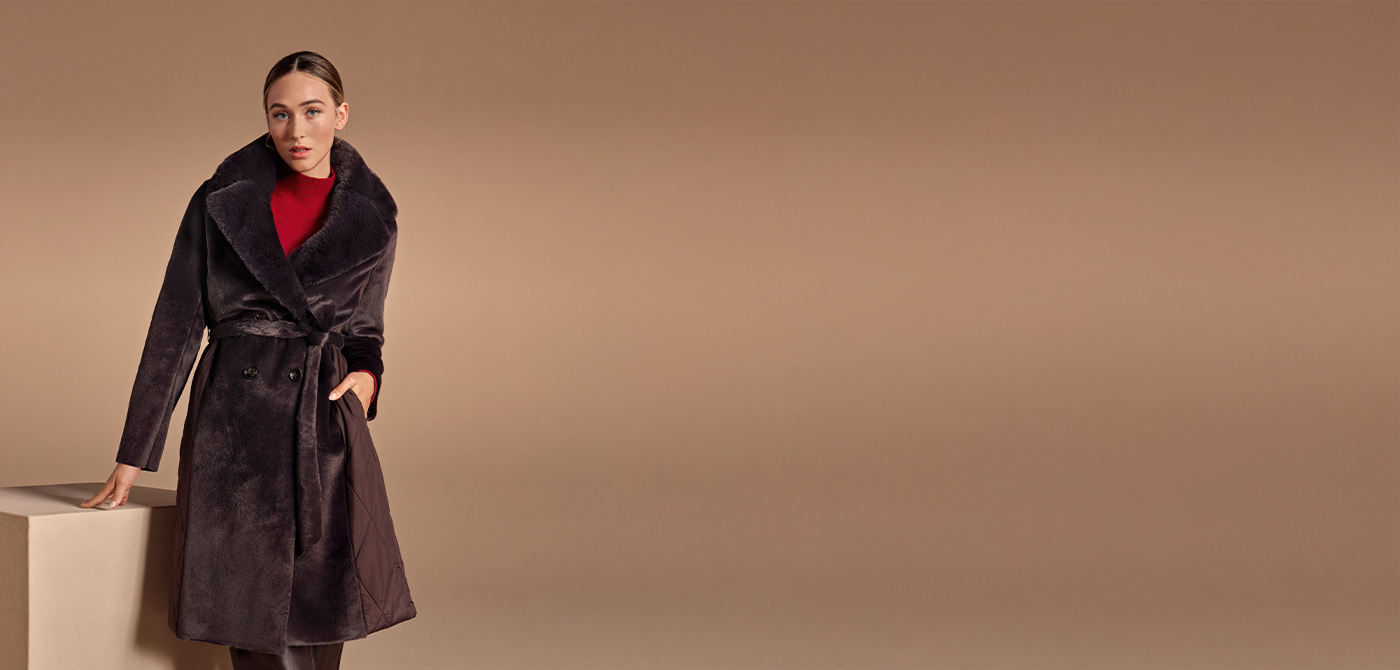 Milestone – Dunkler Fellmantel mit Bindegürtel, kombiniert mit rotem Rollkragen und Lederstiefeln, eleganter Winter-Look.