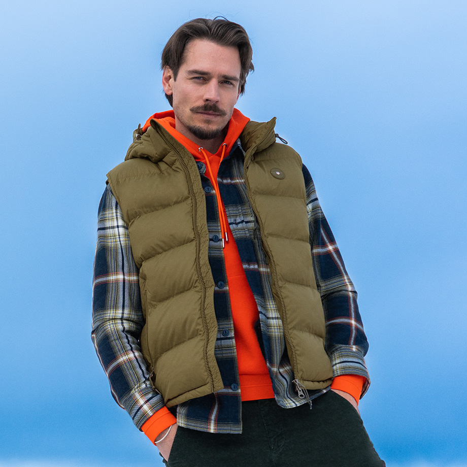 Grüne Steppweste über kariertem Hemd und orangefarbenem Hoodie, lässiger Freizeitlook