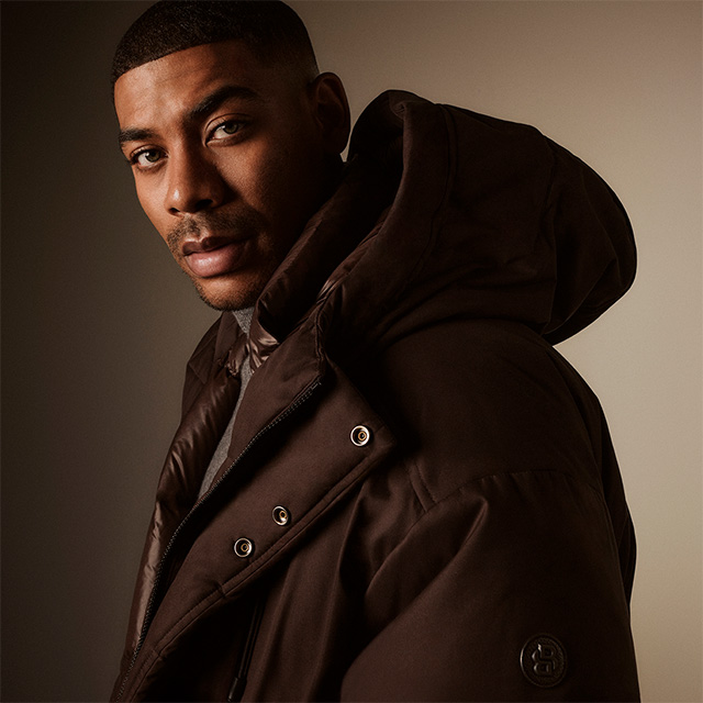 Mann in dunkelbrauner Daunenjacke mit Kapuze, elegant präsentiert
