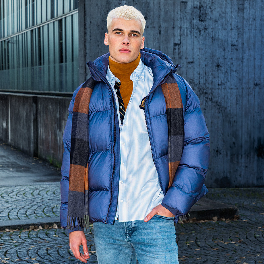 Mann in blauer Daunenjacke mit gestreiftem Schal, Jeans lässig getragen
