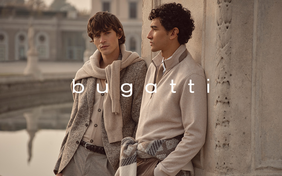 Bugatti: Zwei Männer in beigen Pullovern und karierten Tweedjacken, lässig im Freien getragen.