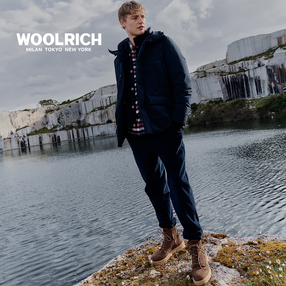 Mann in dunkelblauer Winterjacke und kariertem Hemd, lässig am See stehend