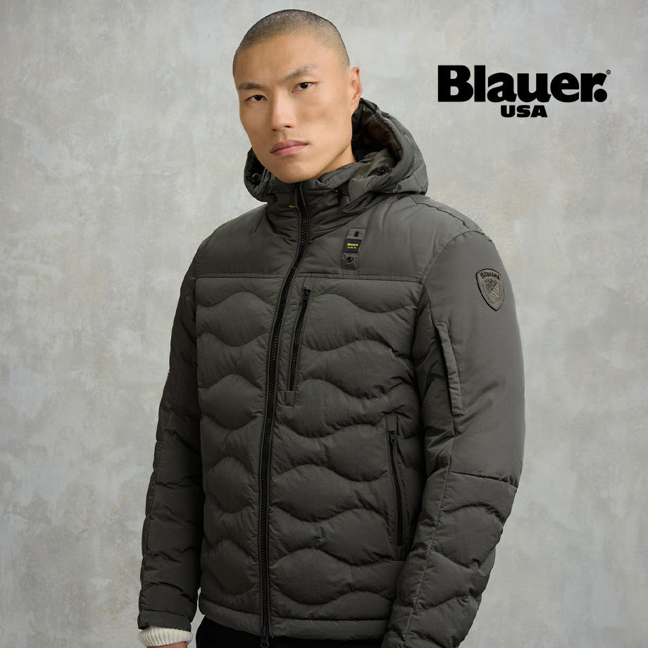 Mann in olivgrüner gesteppter Daunenjacke mit Kapuze, stehend