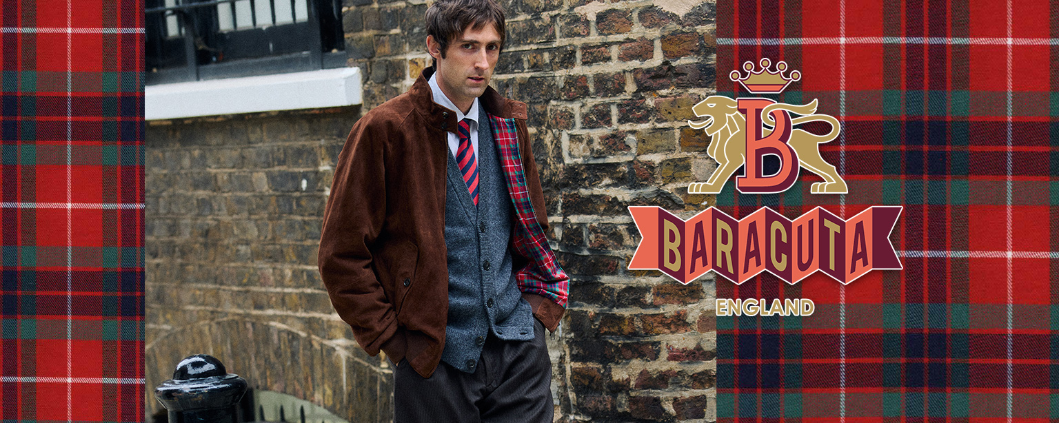 Herr in brauner Suede-Jacke mit grauem Strick-Cardigan und gestreifter Krawatte vor Backsteinhintergrund