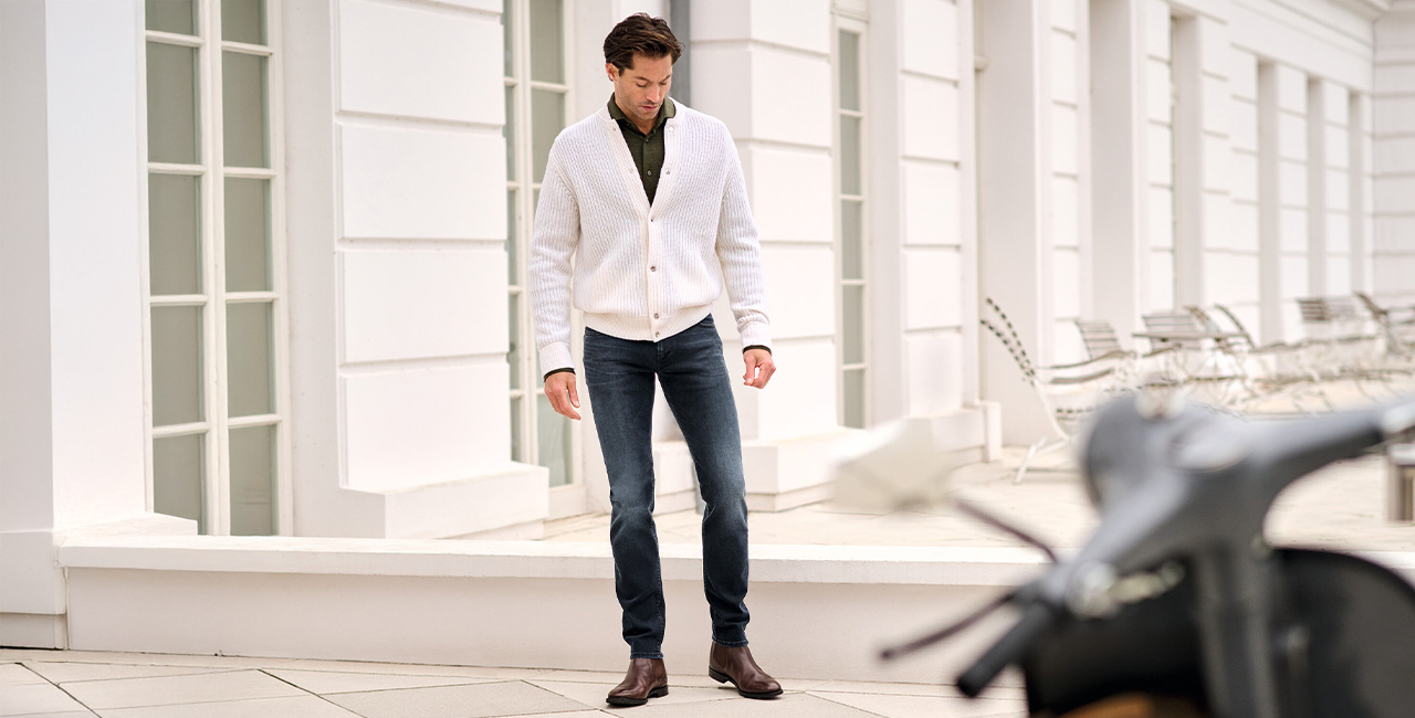 Mann in cremefarbenem Strick-Cardigan und dunkelblauer Jeans, leger im Freien